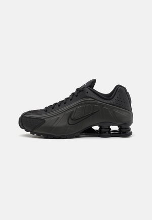 Chaussure de course noire Nike avec un amorti de semelle caractéristique en forme de ressort et un design à lacets, vue de côté sur fond blanc.