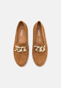 Bruine suede instappers met een gouden kettingaccent over de voorkant. Zachte textuur, ronde neus en flexibele rubberen zool voor comfort.