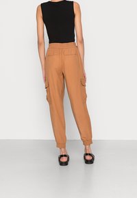 Pantalones cargo en tono beige con cinturilla elástica, puños ajustados y bolsillos laterales para almacenamiento. Combinados con una camiseta de tirantes negra ajustada y sandalias negras.