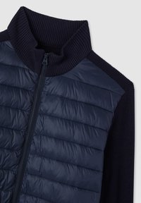 Giacca leggera navy con collo alto a coste e chiusura con zip. Presenta pannello anteriore trapuntato e maniche in maglia testurizzata.
