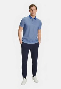 Polo bleu clair avec un col plus foncé, associé à un pantalon bleu marine foncé et des baskets blanches. Manches courtes, texture lisse et coupe ajustée.