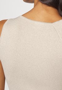 Top beige senza maniche con una texture liscia e metallica. Presenta un collo rotondo e dettagli di cucitura sottili.