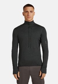 Mężczyzna w ciemnoszarej bluzie z ćwierć zamkiem i otworami na kciuki, stojący prosto na jednolitym białym tle.