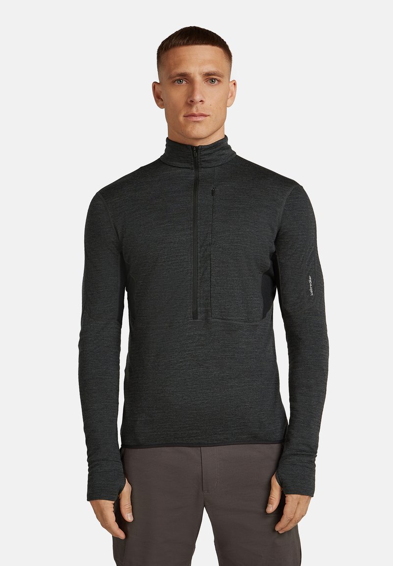 Mężczyzna w ciemnoszarej bluzie z ćwierć zamkiem i otworami na kciuki, stojący prosto na jednolitym białym tle.