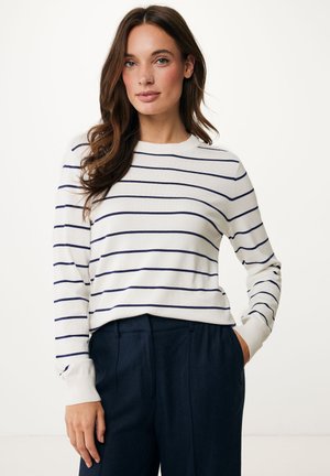 Striped knit sweater in white with navy horizontal stripes, round neckline, long sleeves, and ribbed cuffs, paired with dark trousers.
