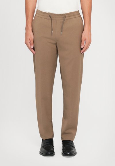 Pantalons de jogging bordeaux effilés avec une taille élastique et un cordon de serrage ajustable, présentant une texture lisse et des poches latérales. Associés à des chaussures noires.
