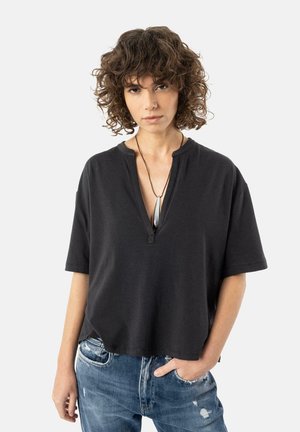 Black short-sleeve top with a v-neck design, featuring a relaxed fit and textured fabric, paired with distressed blue jeans.