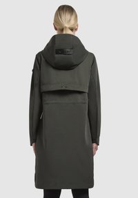 Long, dark green waterproof jacket with a hood, featuring a double-layered back, elastic cuffs, and a subtle logo detail.