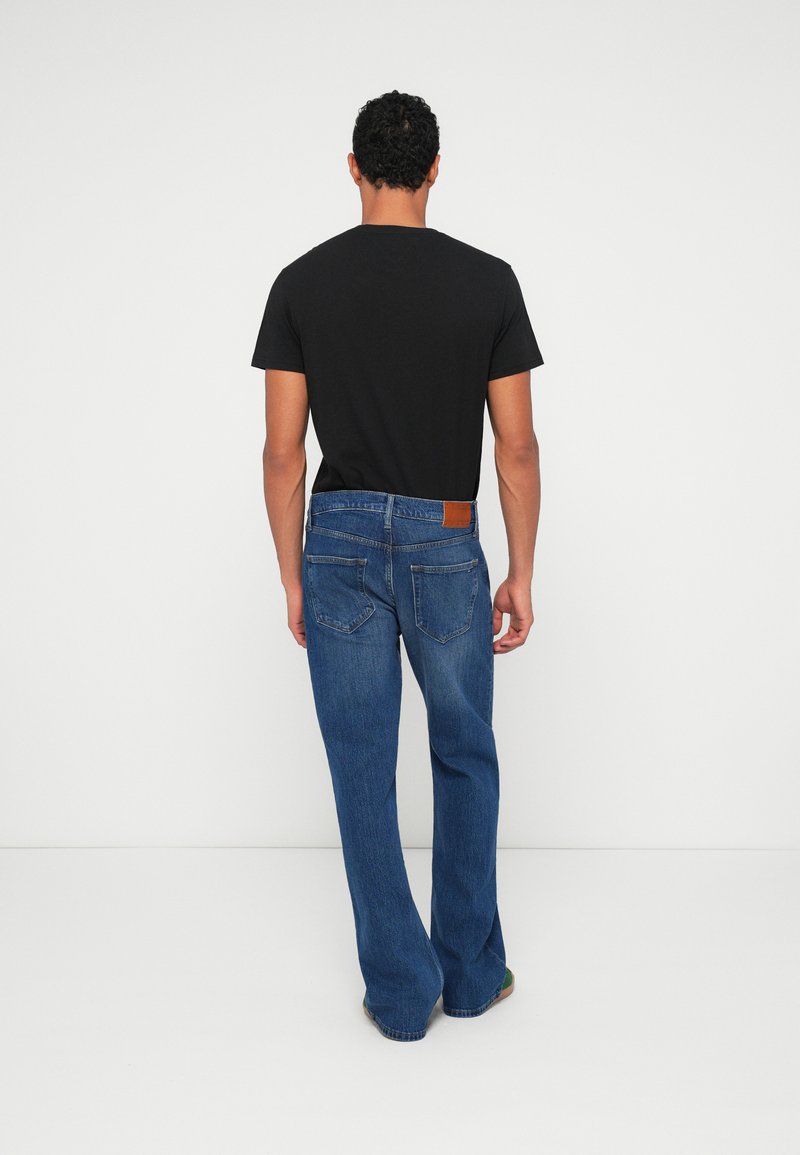 Lys blå jeans med lige ben-design, der har en brun læderlap på den bageste talje og baglommer, parret med en sort t-shirt.