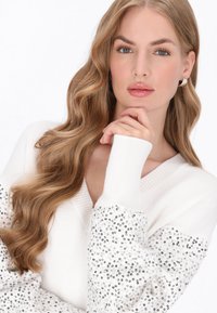 Pulover alb tricotat cu decolteu în V și manșete cu dantelă, cu mâneci decorate cu mărgele. Textură netedă, croială lejeră și accente decorative.