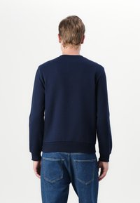 Marineblå bomullssweatshirt med ribbestrikkede mansjetter og nederkant, rund halsdesign, sømløs bakside, kombinert med lyseblå denimjeans.