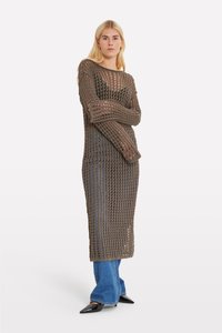 Vestito lungo a maglia aperta marrone con maniche ampie; presenta una vestibilità ampia, un design testurizzato e un look a strati su jeans blu. Scarpa nera a punta.