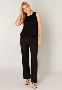 Schwarzes ärmelloses Oberteil mit Rundhalsausschnitt, kombiniert mit locker sitzenden schwarzen Hosen und schwarzen Riemchensandalen. Glatter, leichter Stoff.