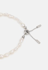 Colier din perle ce prezintă perle albe cu forme neregulate, accesorii din metal argintiu și un închizător tip lanț cu două accente cilindrice.