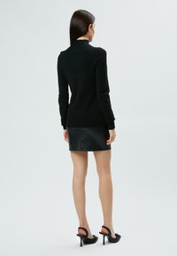 Maglione nero a maglia con collo alto, abbinato a una mini gonna in pelle nera. L'outfit è completato da scarpe con tacco alto nere.