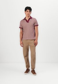 Polo de manga corta en color marrón claro con cuello y puños en marrón oscuro; combinado con chinos beige y zapatillas marrones de cordones.
