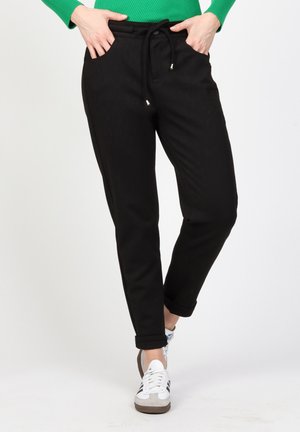 Black tapered joggers with elastic waistband and adjustable drawstring; side pockets; smooth fabric; rolled cuffs. Worn with white sneakers.