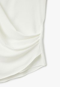 Top bianco in tessuto con una consistenza morbida, caratterizzato da un design drappeggiato e dettagli arricciati sui lati per una forma accentuata.