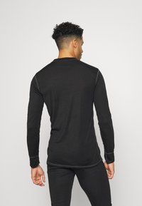 Maglietta nera a maniche lunghe con scollo a girocollo, silhouette aderente e cuciture piatte. Tessuto morbido senza motivi o accenti visibili.