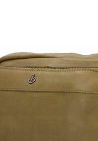 Borsa in pelle marrone con una texture liscia. Presenta un'emblema d'ancora argentata sopra la chiusura con zip, insieme a un dettaglio cucito lungo la cucitura.
