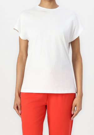 Biała bawełniana koszulka z krótkimi, podwiniętymi rękawami, okrągłym dekoltem i luźnym krojem, zestawiona z jasnoczerwonymi spodniami. Gładka powierzchnia, bez wzorów.