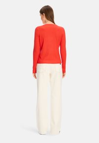 Rippiger, taillierter, roter Pullover mit langen Ärmeln. Kombiniert mit hochgeschnittenen, weit geschnittenen, cremefarbenen Hosen. Minimalistisches Design mit einer glatten Textur.