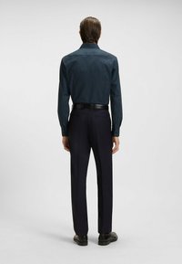 Laivastonsininen kuvioitu paita, jossa on pieniä valkoisia pisteitä, pitkät hihat ja levitetty kaulus, yhdistettynä muotoiltuihin mustiin housuihin.