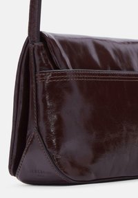 Borsa a mano in pelle marrone scuro con finitura liscia, design angolare, cuciture a contrasto e un logo sottile impresso vicino alla base.