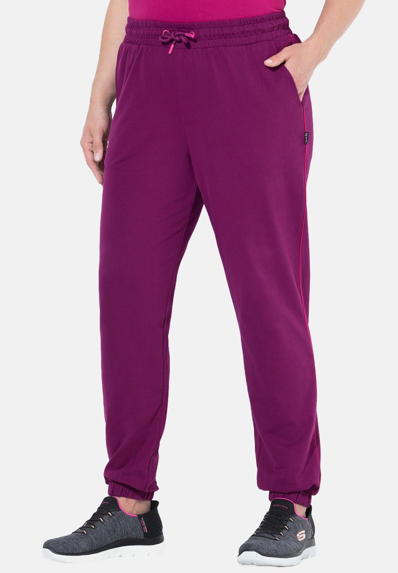 Lila Sporthosen mit elastischem Bund, Kordelzug, Seitentaschen und schmal zulaufenden Bündchen, kombiniert mit schwarzen und rosa Sneakers.