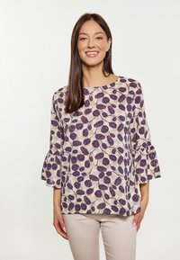 Blusa ampia in tessuto leggero, con sfondo color crema e motivo di foglie viola, dotata di maniche a campana. Abbinata a pantaloni beige.