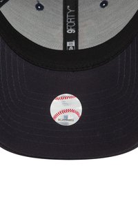 Gorra de béisbol negra con una pegatina metálica redonda que presenta un diseño de béisbol. Material de algodón, forma estructurada, visera plana y forro interior visible.