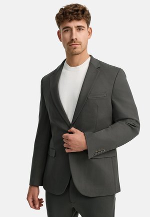 Blazer gris oscuro de tela suave, con un bolsillo en el pecho y puños abotonados, usado sobre un suéter blanco de cuello redondo.