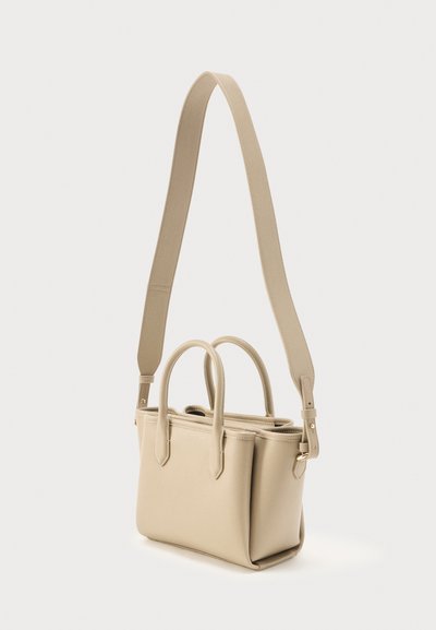 Μπεζ δερμάτινη τσάντα χειρός με δύο κορυφαίες λαβές και ρυθμιζόμενο, φαρδύ ιμάντα ώμου σε απλό φόντο.