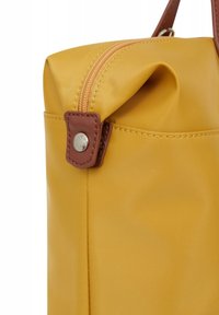 Geel nylon tas met een gestructureerde afwerking, slank ontwerp, bruine leren accenten en een zichtbare rits met een metalen trekker.