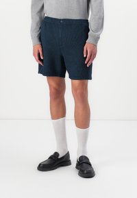 Dark blue, textured shorts with elastic waistband and button closure, paired with white crew socks and black slip-on shoes.