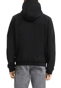 Must and drawstringiga musta kapuutsi särk, mille ülemises seljaosas on õmmeldud õmblus. Selga pandud hallide denimpükstega, millel on tagataskud.