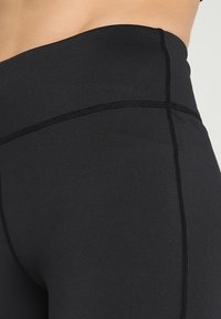 Leggings sportivi neri con un alto punto vita, realizzati in tessuto liscio ed elasticizzato, dotati di cuciture piatte e una silhouette aderente.