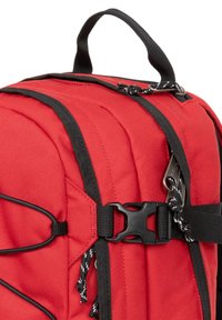 Sac à dos rouge avec accents noirs, doté d'une finition texturée, de plusieurs sangles, d'une poignée robuste et d'une boucle en plastique pour une fermeture sécurisée.