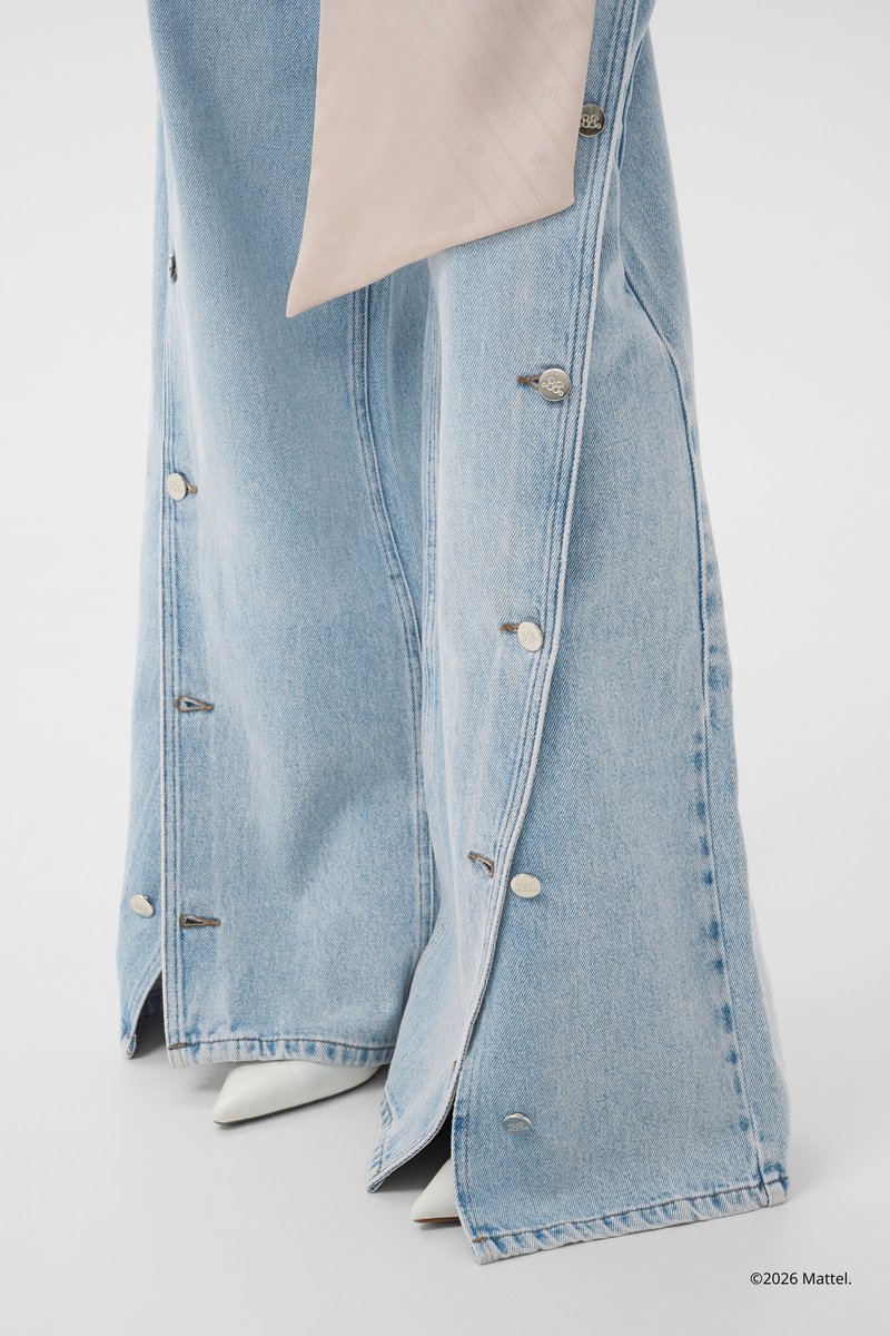 Lyseblå vidde denim-bukser med trykknapper langs siderne, kombineret med hvide spidse sko og en lysebeige taske.