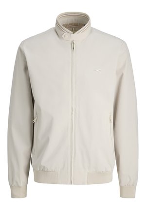 Jachetă bej cu fermoar, guler drept, manșete și tiv striate, două buzunare laterale cu fermoar și un logo subtil pe piept.