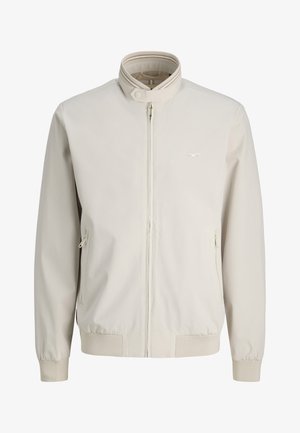Beige Reißverschlussjacke mit Stehkragen, gerippten Bündchen und Saum, zwei seitlichen Reißverschlusstaschen und dezentem Logo auf der Brust.