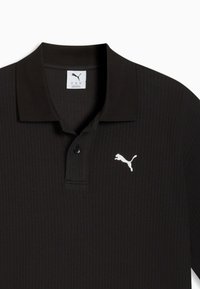 Schwarzes, geripptes Poloshirt mit zwei Knöpfen und weißem Puma-Logo auf der linken Brust, dargestellt auf weißem Hintergrund.