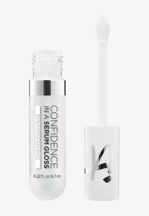 Tube transparent de gloss étiqueté « Confiance dans un gloss sérum », avec une baguette applicatrice à côté, montrant la texture et le volume du produit.