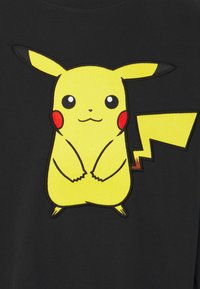 Černé tričko z látky s výšivkou žlutého Pikachu designu, s červenými tvářemi, velkýma očima a vzorem cik-cak ocasu.