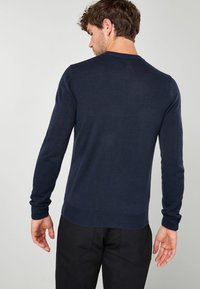 Suéter de punto azul marino con cuello redondo, mangas largas y puños y dobladillo acanalados. Textura suave, diseño ajustado y estilo minimalista.