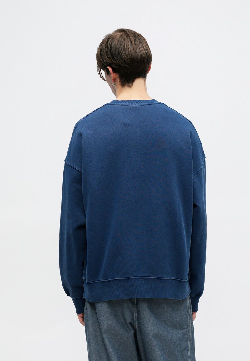 Dunkelblaues Sweatshirt mit Rundhals, lockerer Passform und gerippten Bündchen. Weicher Baumwollstoff, minimale Nähdetails auf der Rückseite.