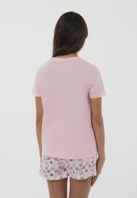 T-shirt di cotone rosa chiaro con maniche corte. Abbinata a pantaloni corti bianchi con un motivo di caramelle colorate, comprese le lecca-lecca e i fiori.