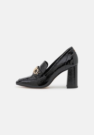 Chaussure à talon haut en cuir verni noir avec un bout pointu, un accent en métal doré et une finition texturée sur la tige.