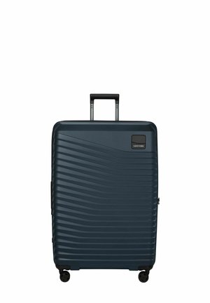 Valise rigide bleu marine avec des vagues horizontales texturées, quatre roues pivotantes et une poignée télescopique étendue.