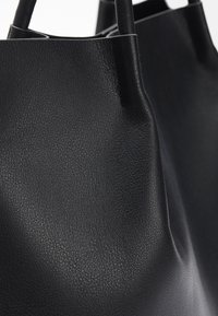 Gros plan d’un sac fourre-tout en cuir noir texturé avec des poignées arrondies et une finition lisse.